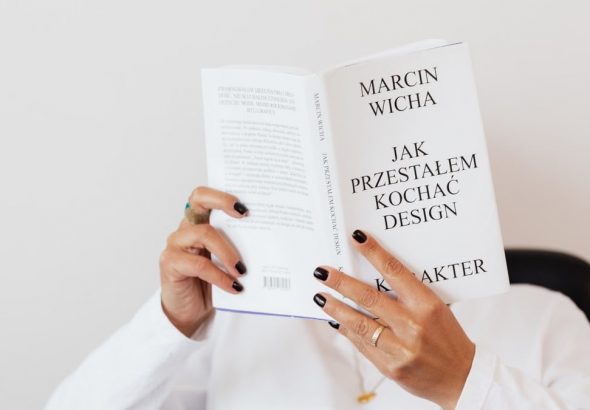 Anonymous female in white shirt with gold chain on neck reading interesting book covering face while sitting on black chair