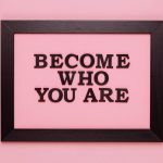 Inspiring quote 'Become Who You Are' framed on a vibrant pink wall, perfect for encouragement.