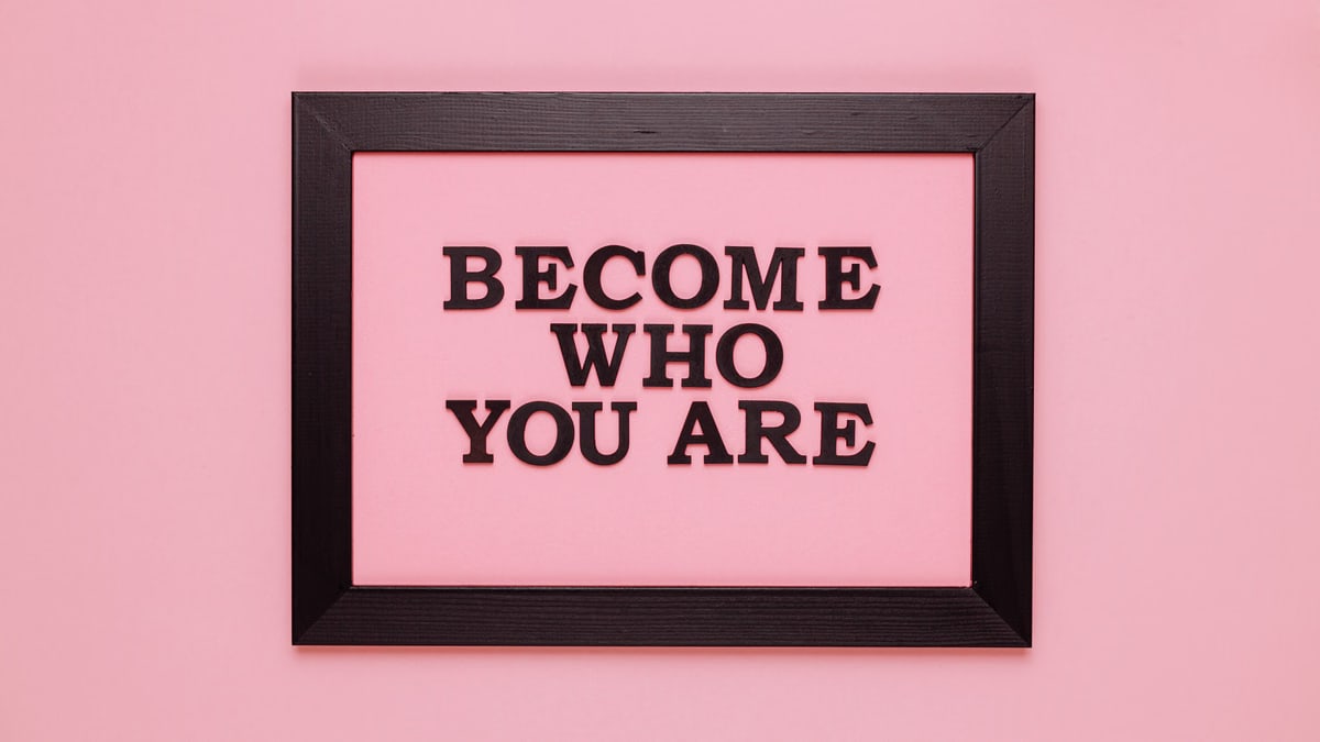 Inspiring quote 'Become Who You Are' framed on a vibrant pink wall, perfect for encouragement.